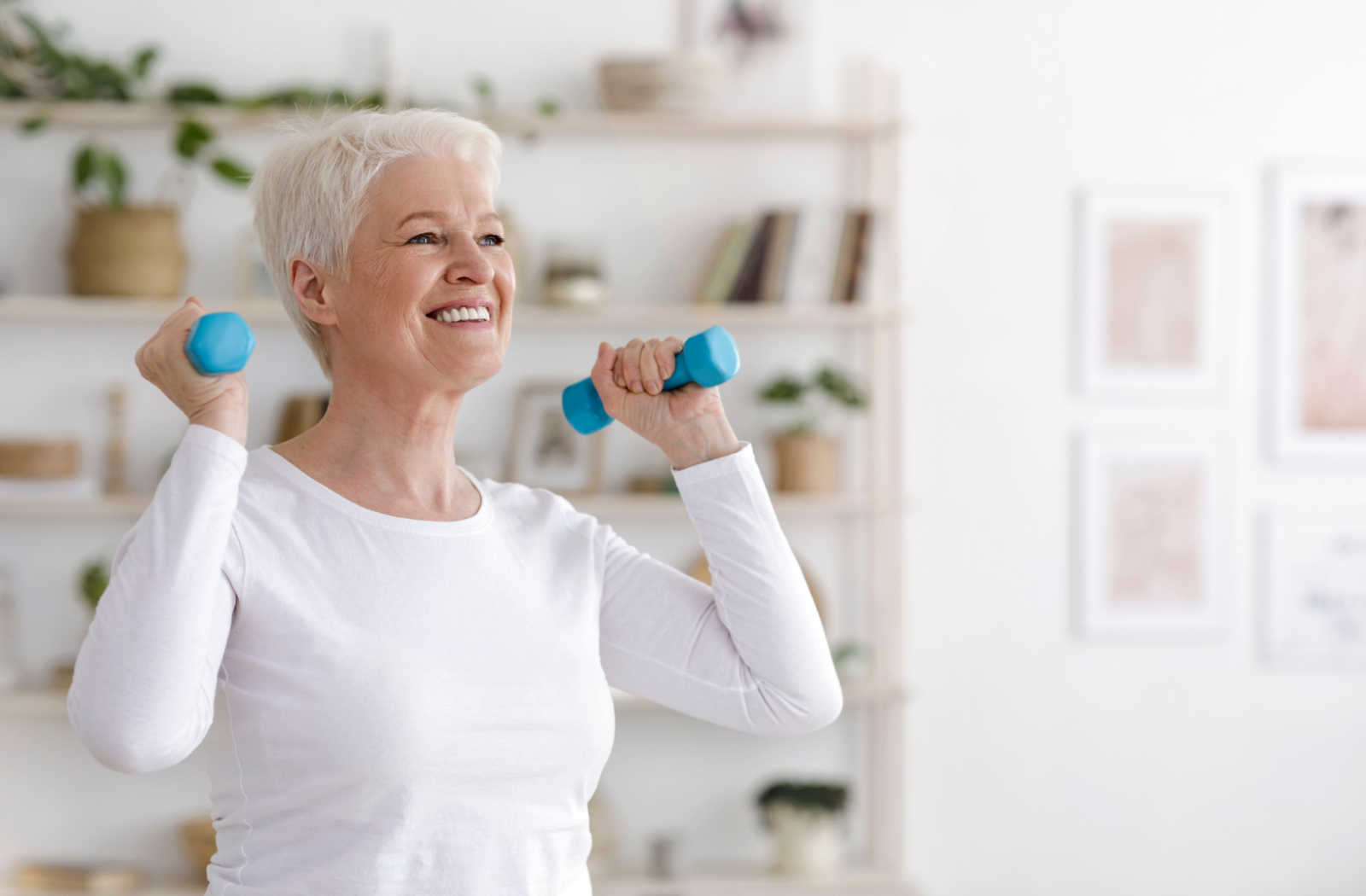 A smiling senior wearing fitness clothes and exercising with dumbbells.