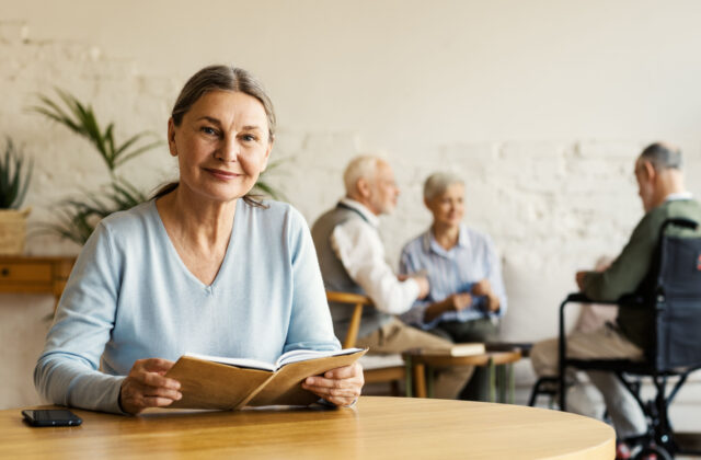 A senior woman with gray hair looking directly at the camera smiling and holding a book