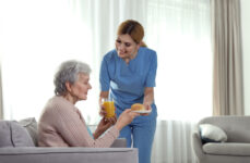 A female nurse assisting a senior woman and serving her orange juice and a croissant