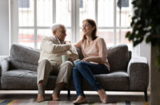 A senior man sitting with his daughter on the couch and smiling away as they enjoy a healthy conversation about moving.