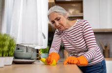 A senior woman wearing gloves and cleaning a table.