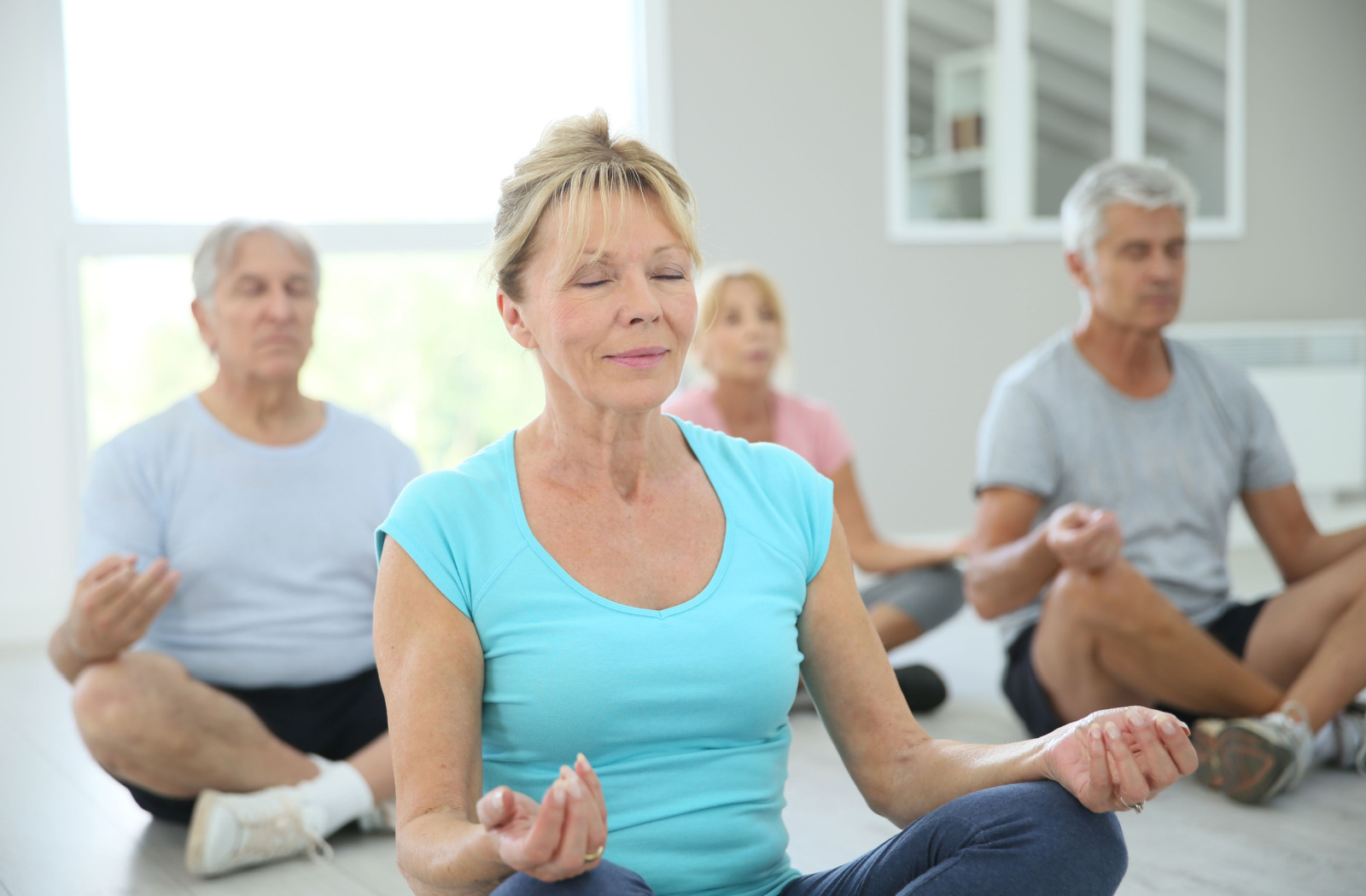 A group of older adults with closed eyes practicing yoga and sitting on yoga mats