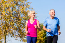 An older adult man and a woman smiling while jogging outdoors.