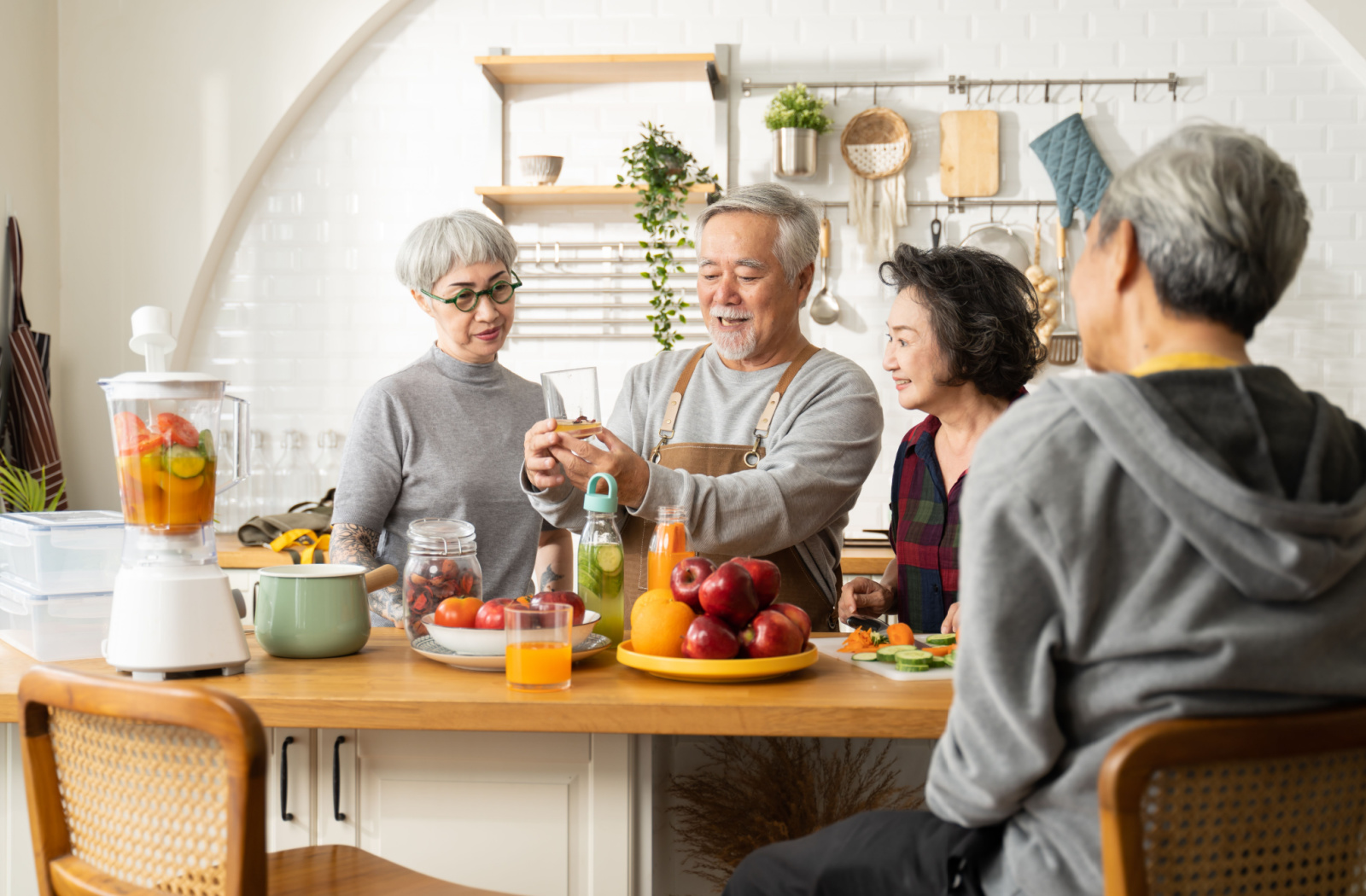 A group of older adults standing around a kitchen island that's filled with fruits, vegetables, and a blender, making fruit-infused water and smoothies